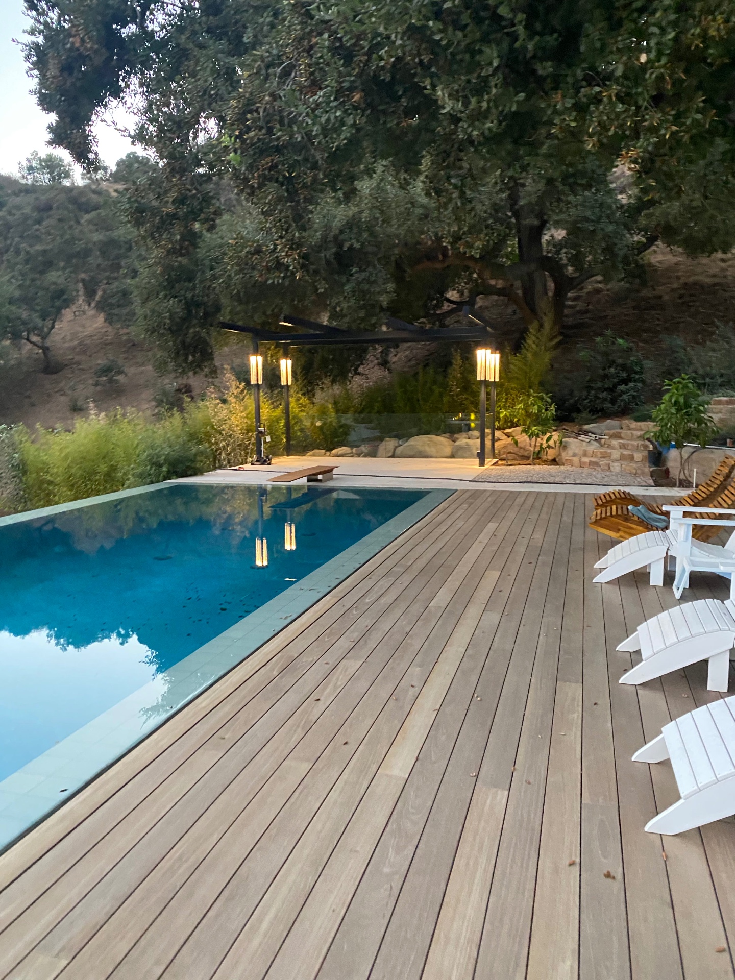 Completed wood pool deck with pergola and landscape lighting at a hillside outdoor living project