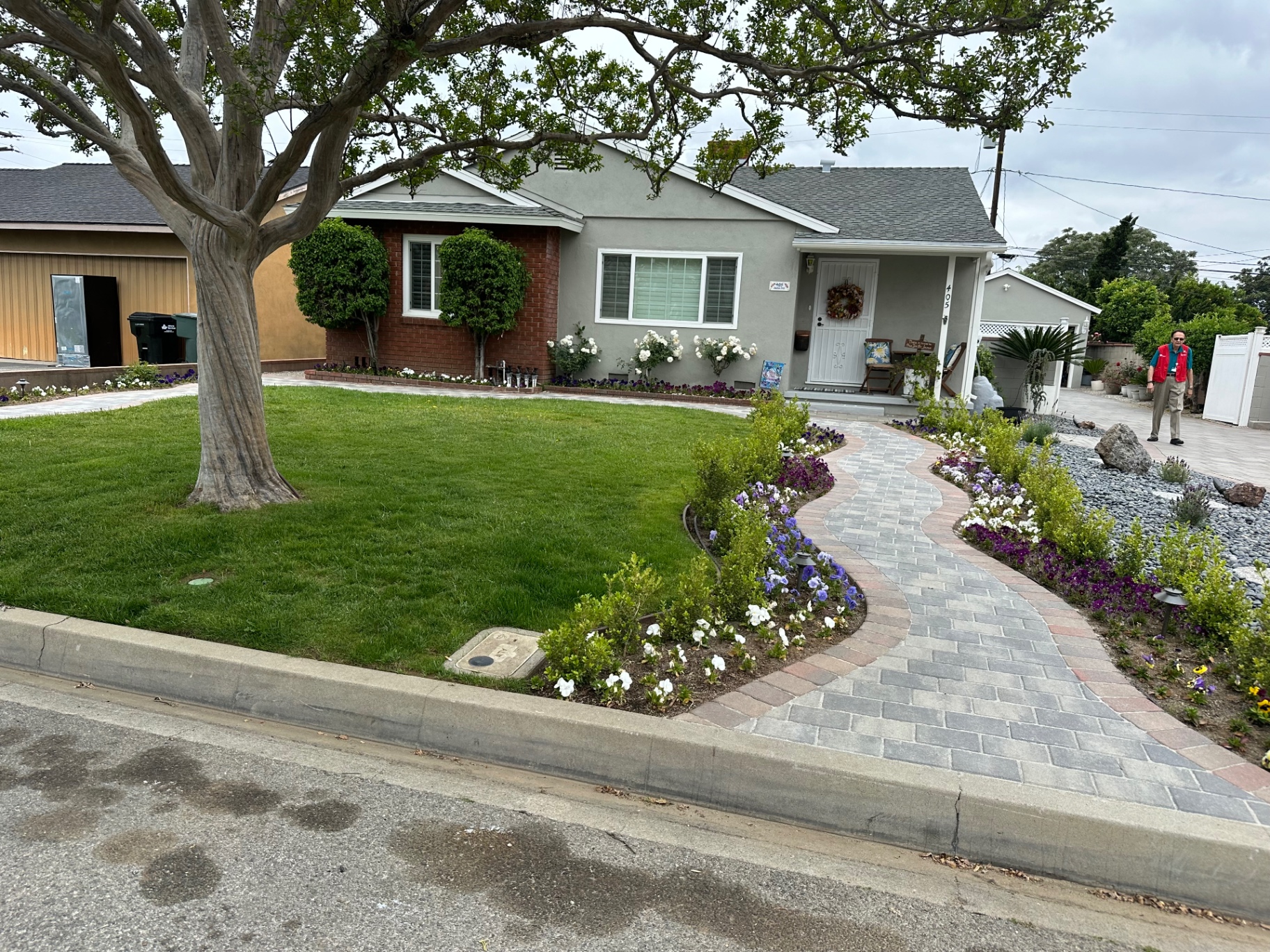 Completed curved paver walkway through a flower-lined front yard landscaping project with manicured lawn