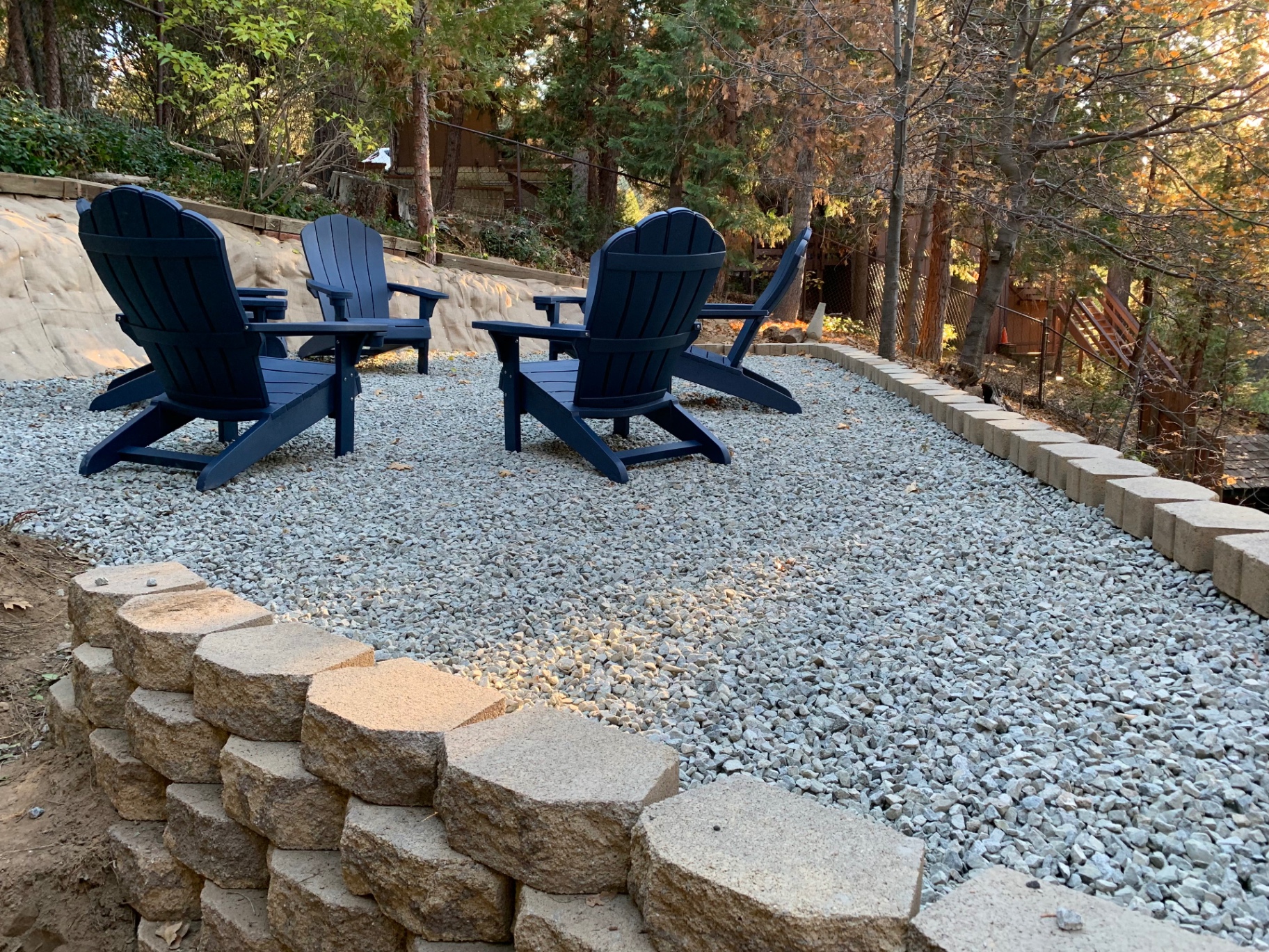 Completed gravel patio seating area framed by a stacked-stone retaining wall in a wooded backyard